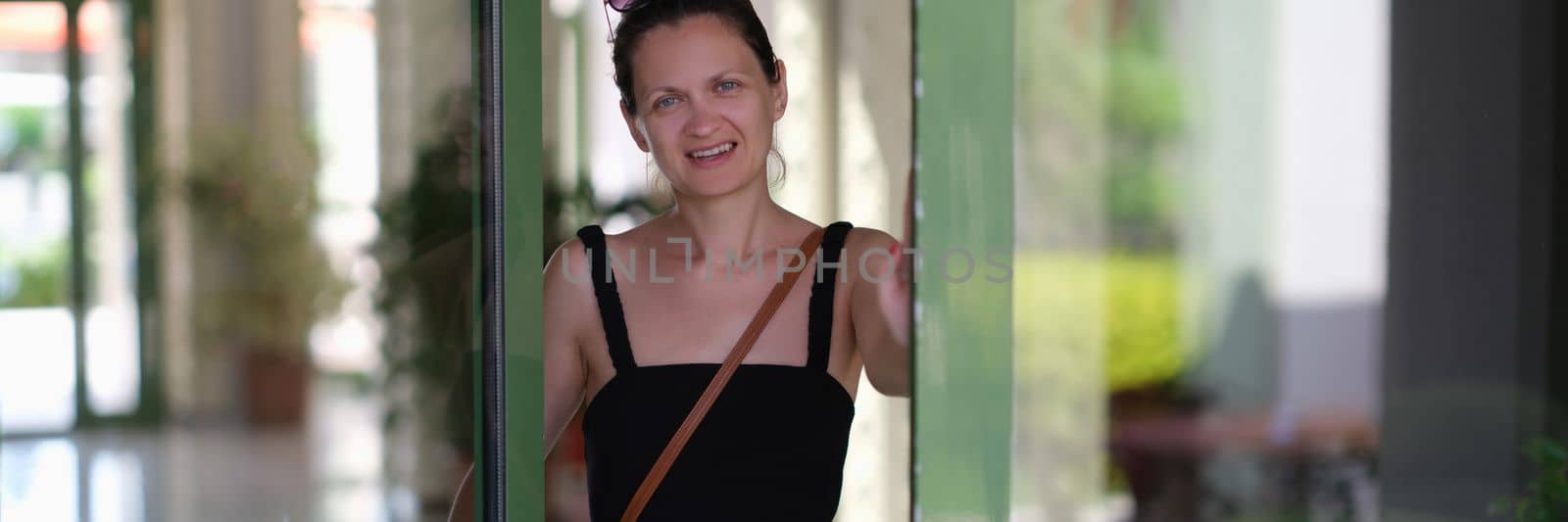Young smiling woman opens a glass door. Meeting guests concept
