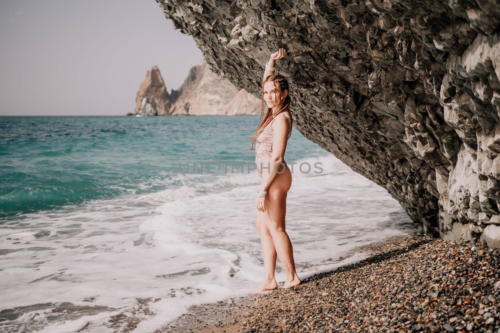 Beach vacation. Hot beautiful woman in sunhat and bikini standing with her arms raised to her head enjoying looking view of beach ocean on hot summer day.