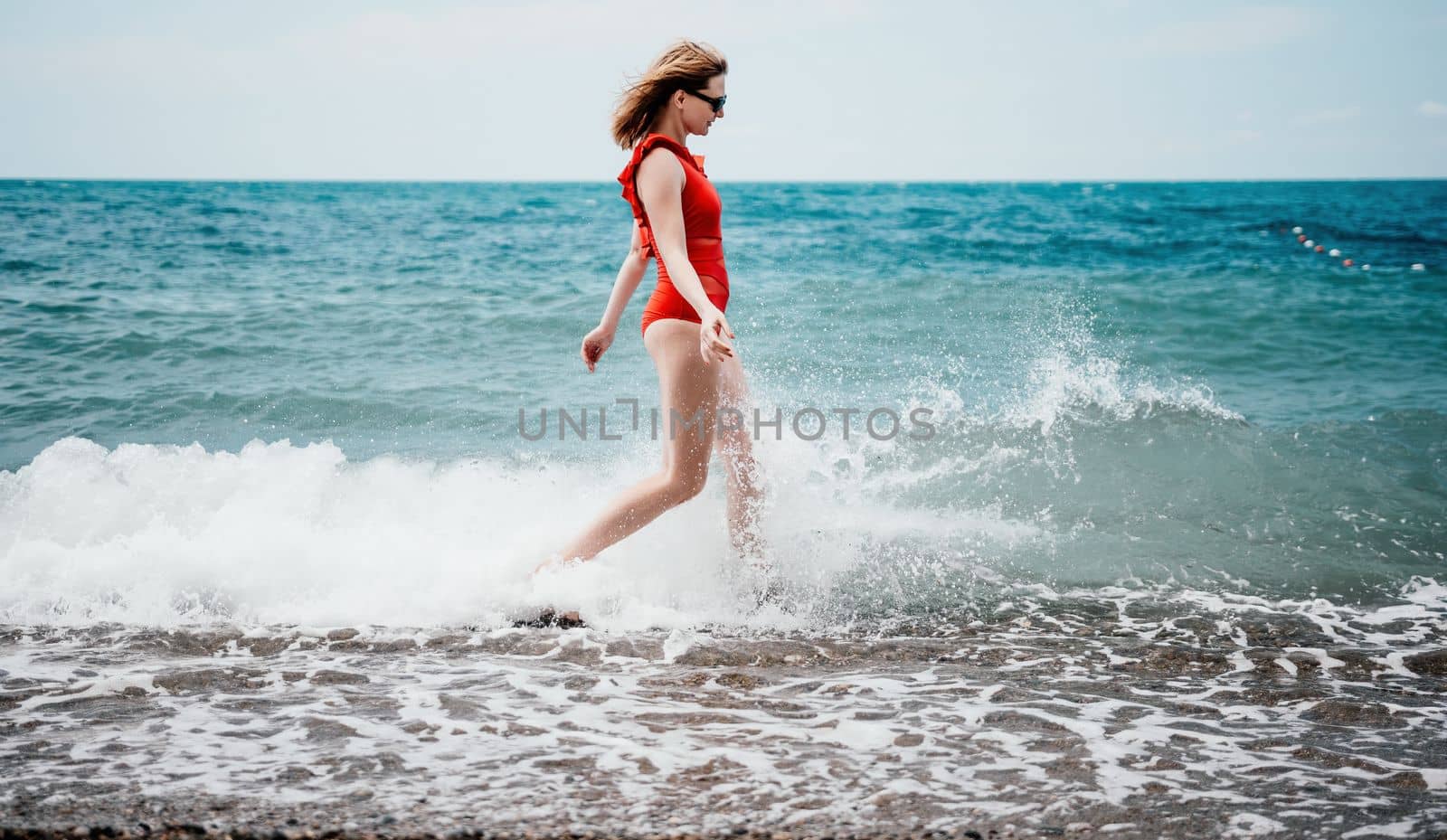 Young happy woman walks carefree on the seaside. Happy lady in red bikini. Portrait beautiful young woman relax smile around beach sea ocean in holiday vacation travel trip.