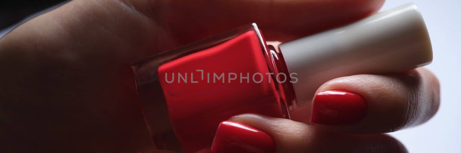 Hands with red manicure and bottle of nail polish. Beautiful stylish nails concept