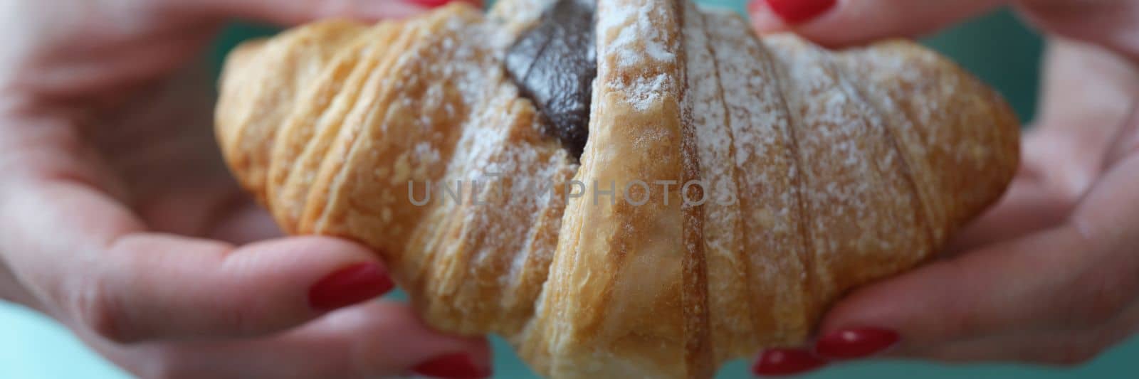 Hand shows a fresh croissant with chocolate and powdered sugar. Fresh sweet croissant concept