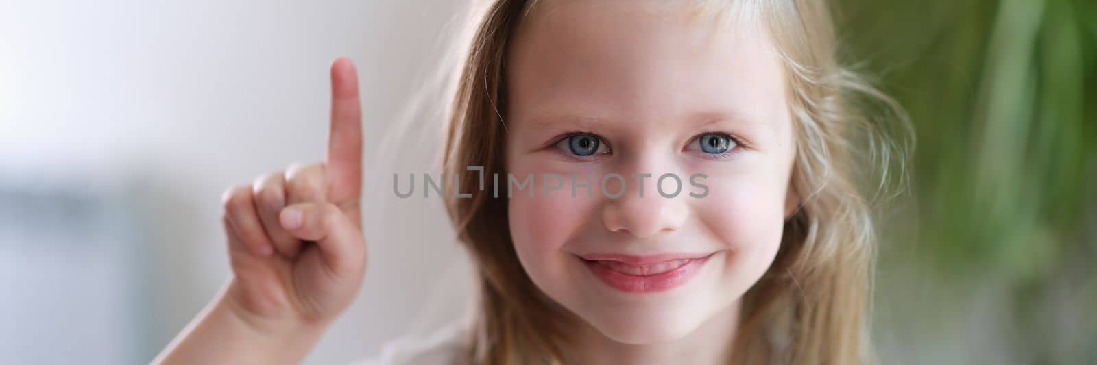 Portrait of beautiful little smiling baby girl holding thumbs up. Creative creative baby ideas concept