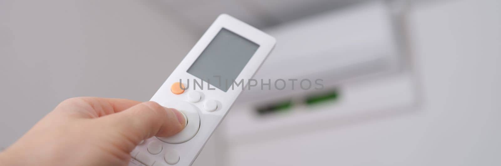 Hand with remote control is directed to air conditioner on wall by kuprevich