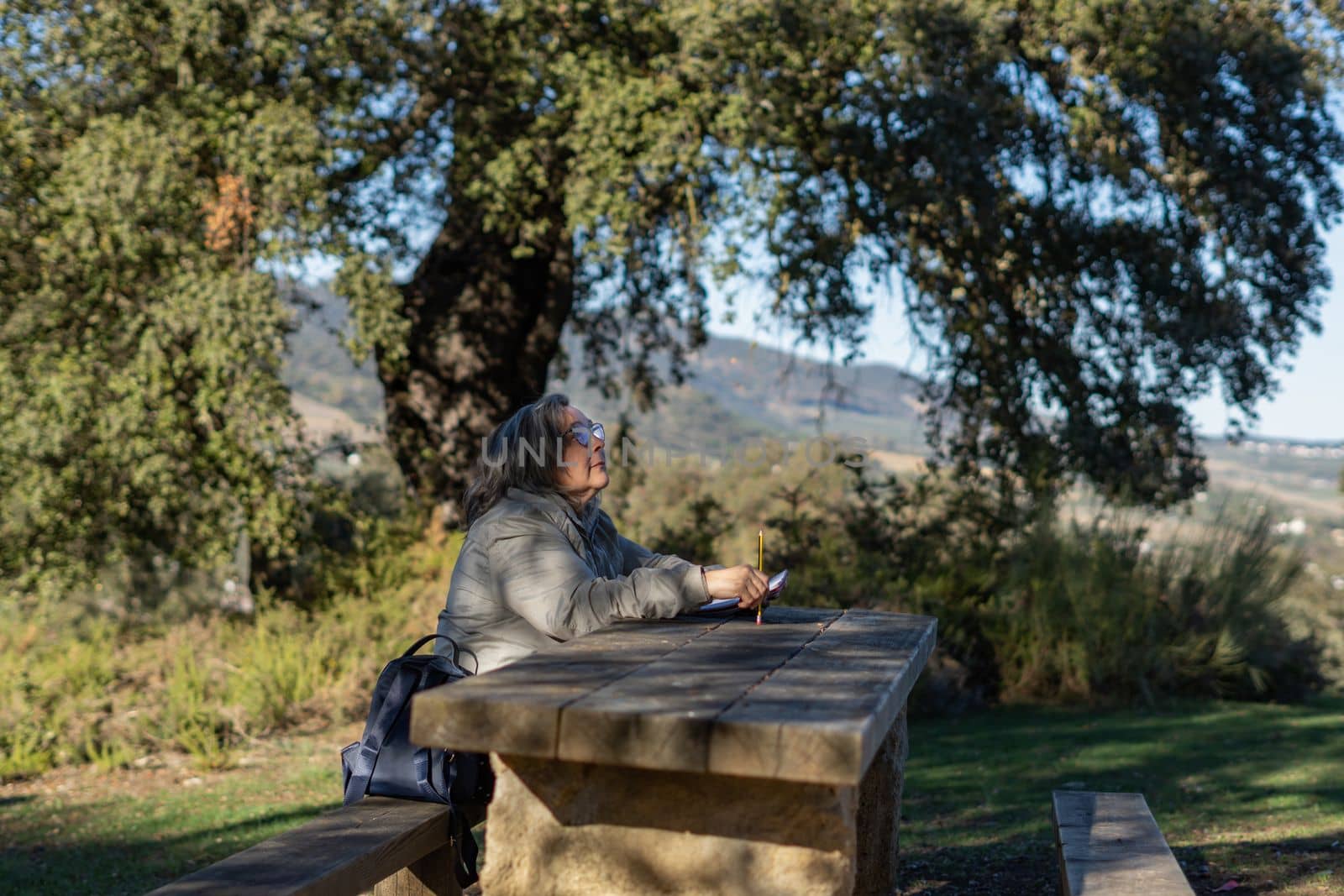 white-haired woman with glasses taking notes in her notebook in the park on a sunny winter's day