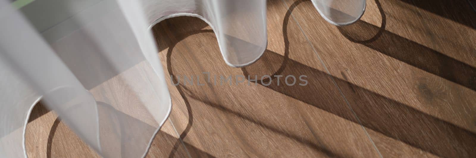 White curtains in midday sun create shade on brown wood floor in room by kuprevich