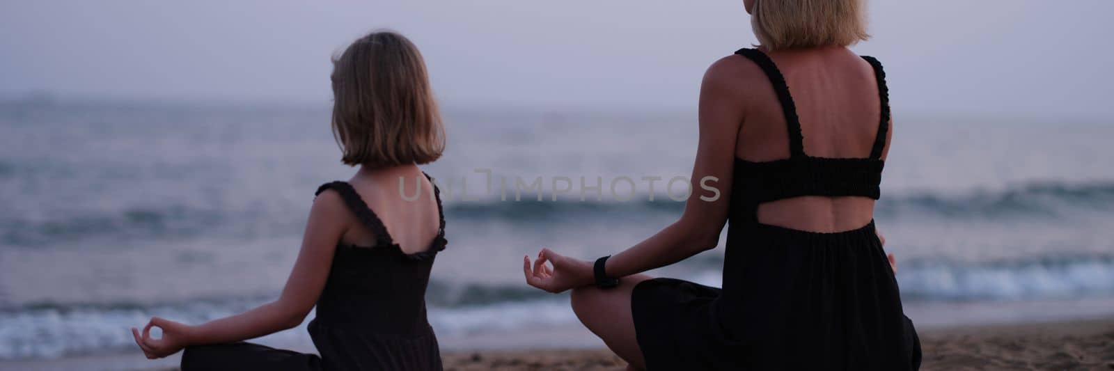 Mom and daughter do yoga and meditate on beach by kuprevich