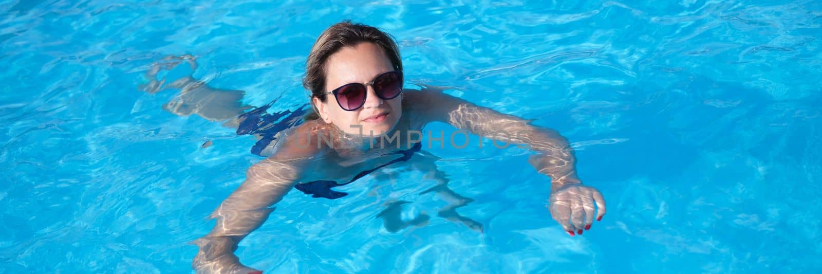 Woman in sunglasses swims in pool in summer by kuprevich