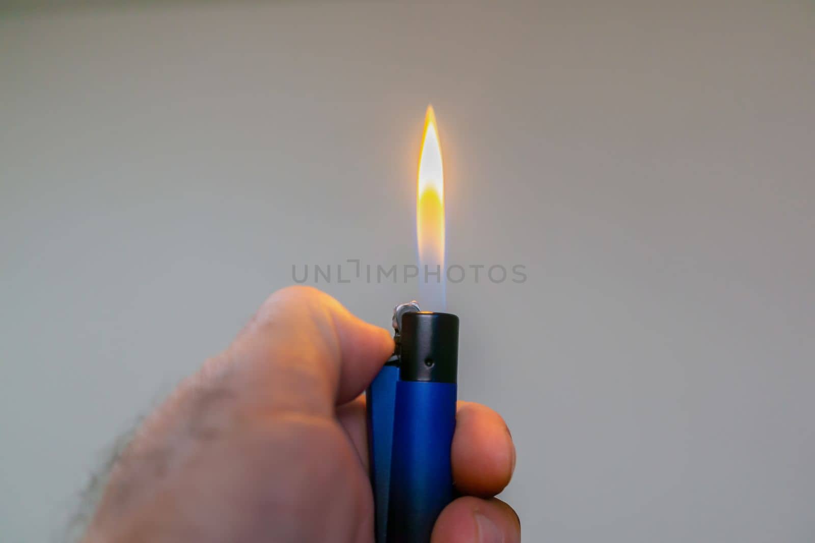 man's hand lighting a blue lighter with copy space and light background