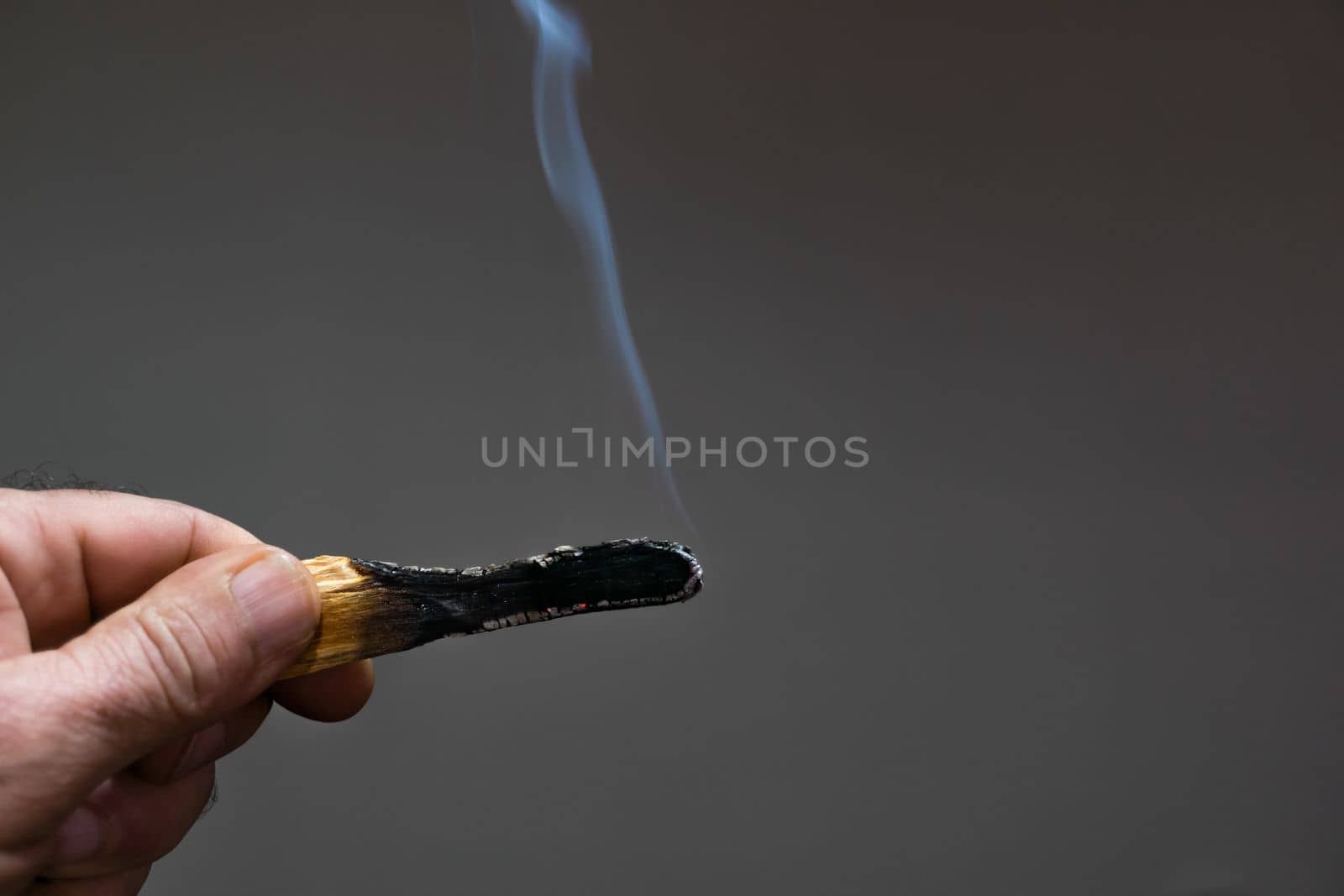 man's hand holding a piece of burning and smoldering palo santo with dark background and copy space