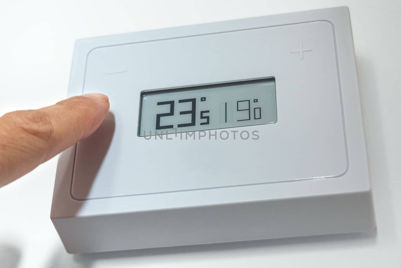 Lowering the temperature of a home thermostat due to energy crisis. Close up.