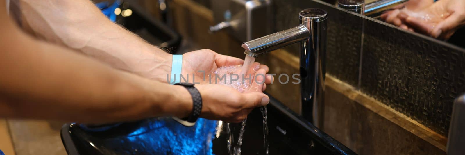 Man washes hands in the sink in bathroom at home checking temperature by touching running water with hand by kuprevich