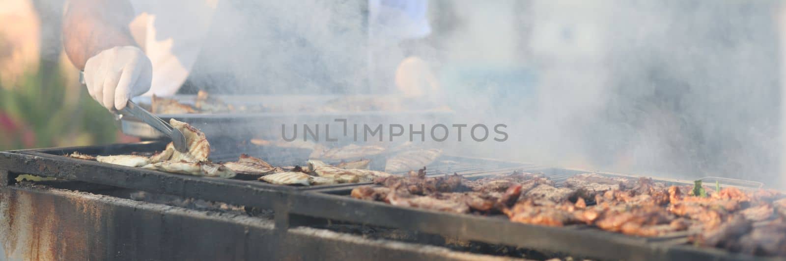 Cook prepares fish and meat on grill in market or cafe. Cooking food on grill in hotels concept