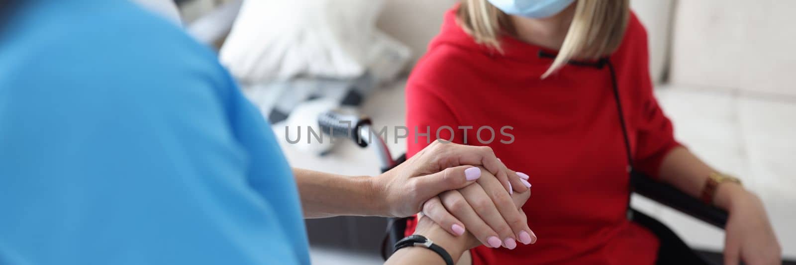 Rehabilitation doctor in protective medical mask communicates with disabled woman in wheelchair. Rehabilitation and treatment in hospice concept