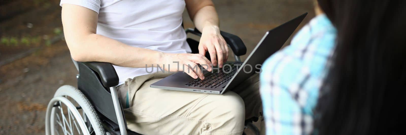 Man in wheelchair and woman work remotely while sitting in park by kuprevich