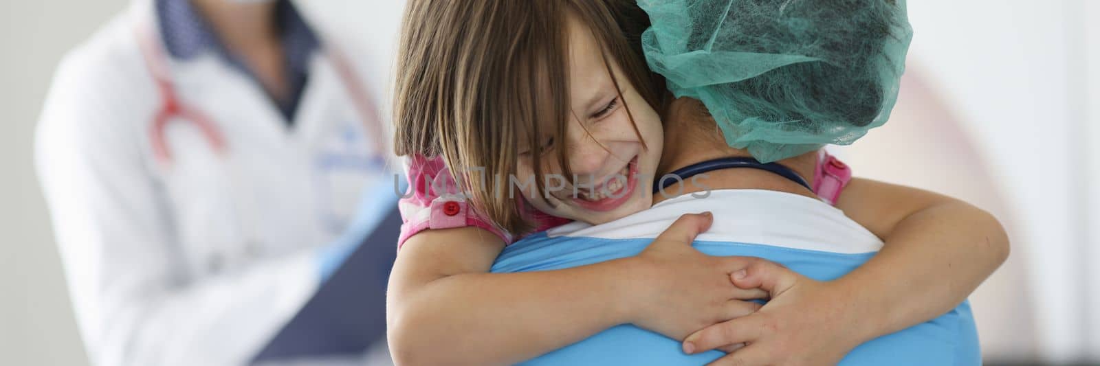 Doctor holds frightened little child girl in arms in clinic. Children fear of injections concept