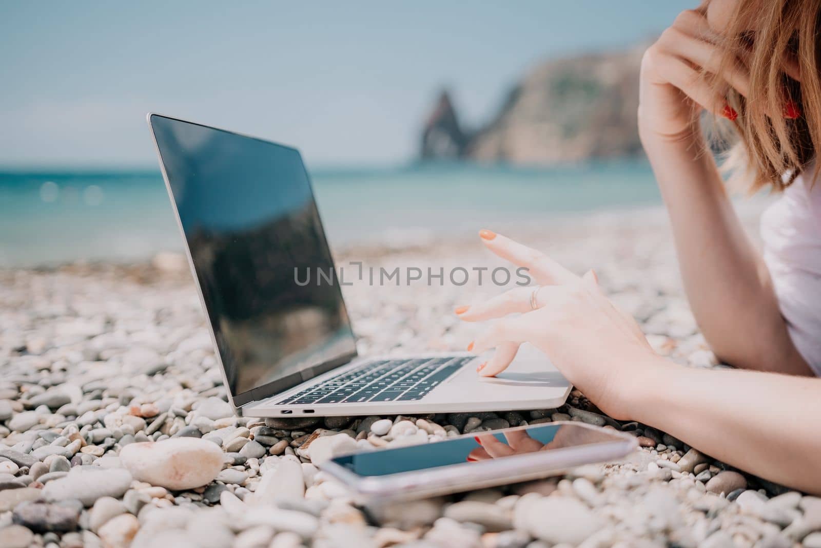 Woman sea laptop. Business woman in yellow hat working on laptop by sea. Close up on hands of pretty lady typing on computer outdoors summer day. Freelance, digital nomad, travel and holidays concept. by panophotograph