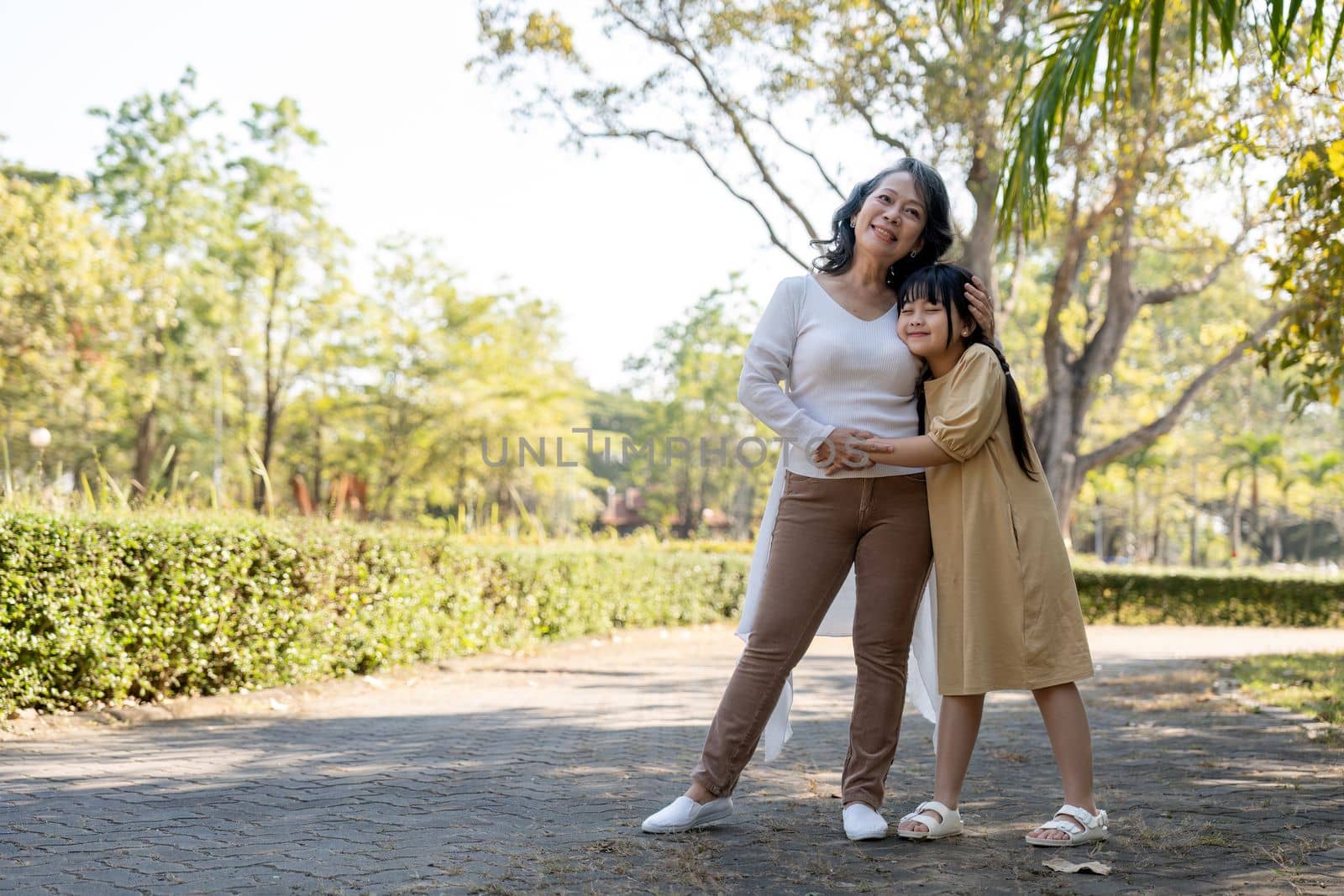 Happy granddaughter and hug her grandmother at summer park, family, leisure and people concept by nateemee