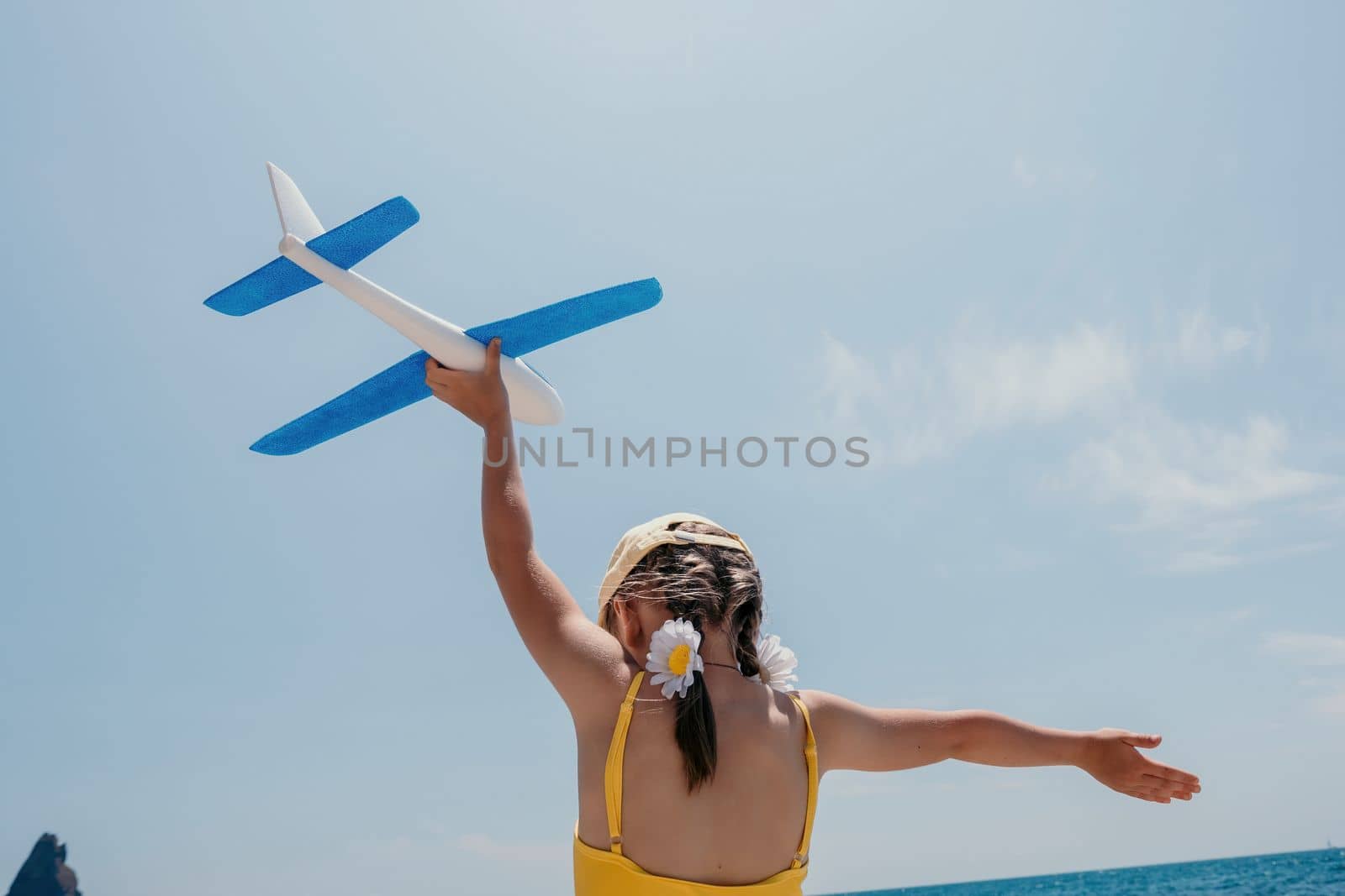 Kid playing with toy airplane. Children dream of travel by plane. Happy child girl has fun in summer vacation by sea and mountains. Outdoors activities at background of blue sky. Lifestyle moment. by panophotograph