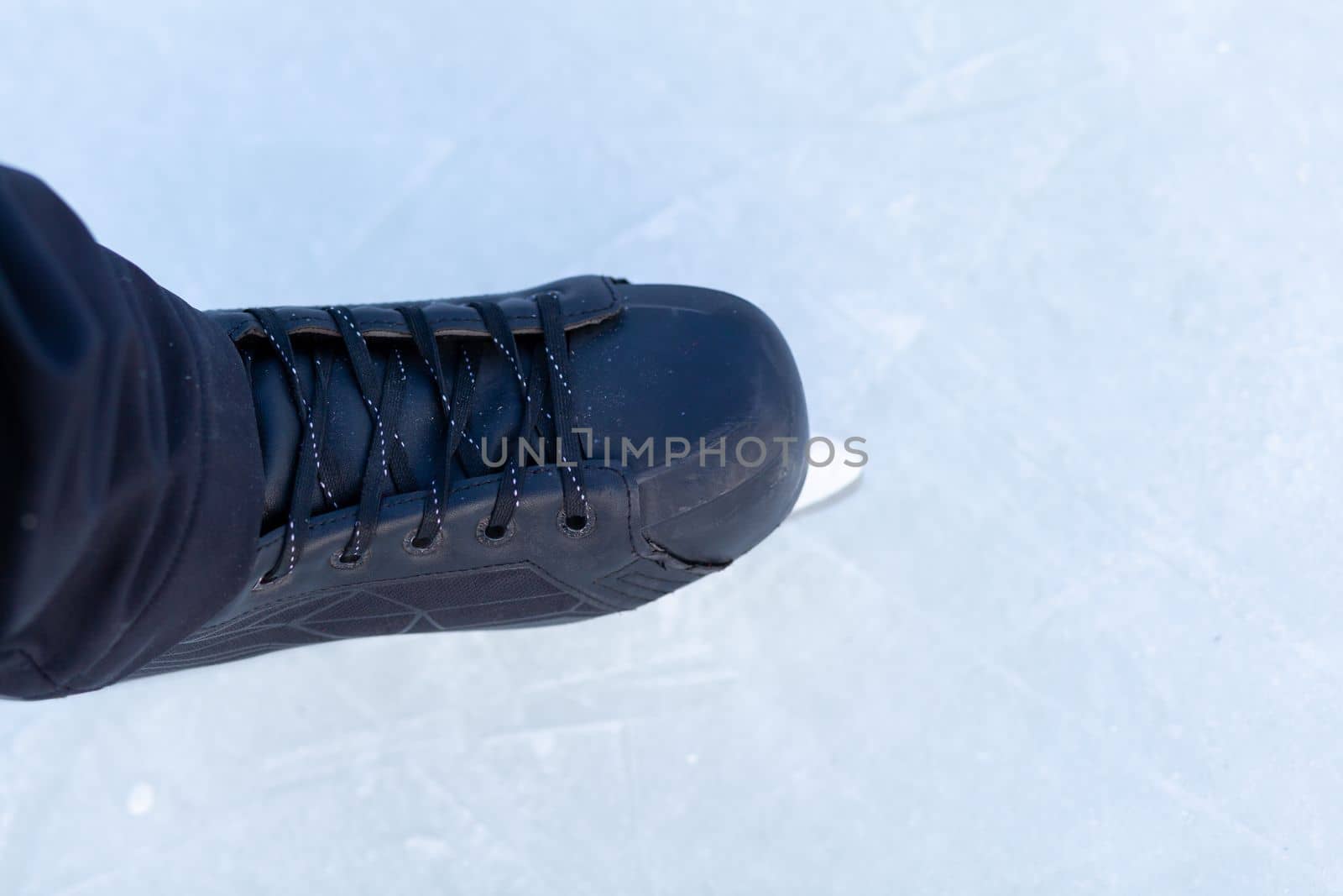 A pair of hockey skates with laces on frozen ice rink closeup. Ice skating or playing hockey in winter. ice and legs and copy space over ice background with marks from skating