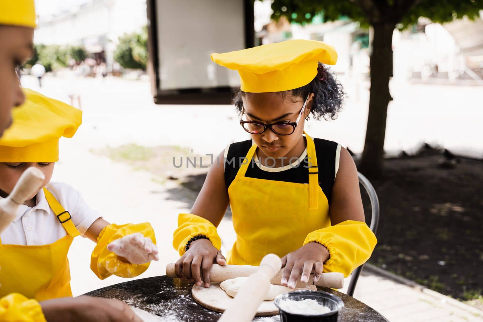 Multiethnic cooks children in yellow chefs hat and apron cooking dough for bakery. Black african and caucasian child cooking and having fun together