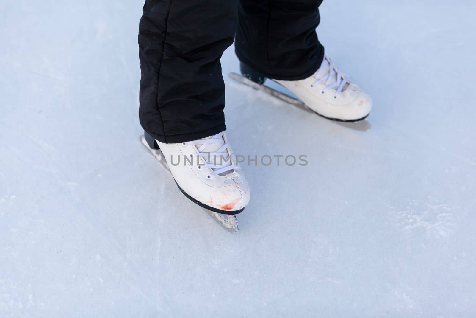 A pair of hockey skates with laces on frozen ice rink closeup. Ice skating or playing hockey in winter. ice and legs and copy space over ice background with marks from skating