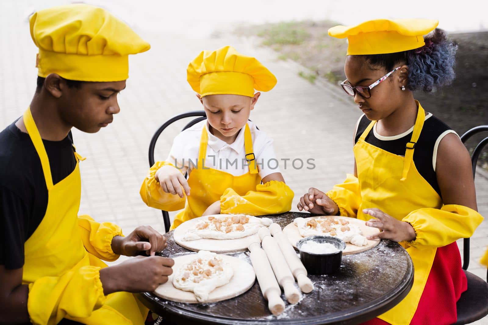 Happy company of multiethnic children cooking dough. Childhood cook activity of multinational children of black african and caucasian kids. by Rabizo