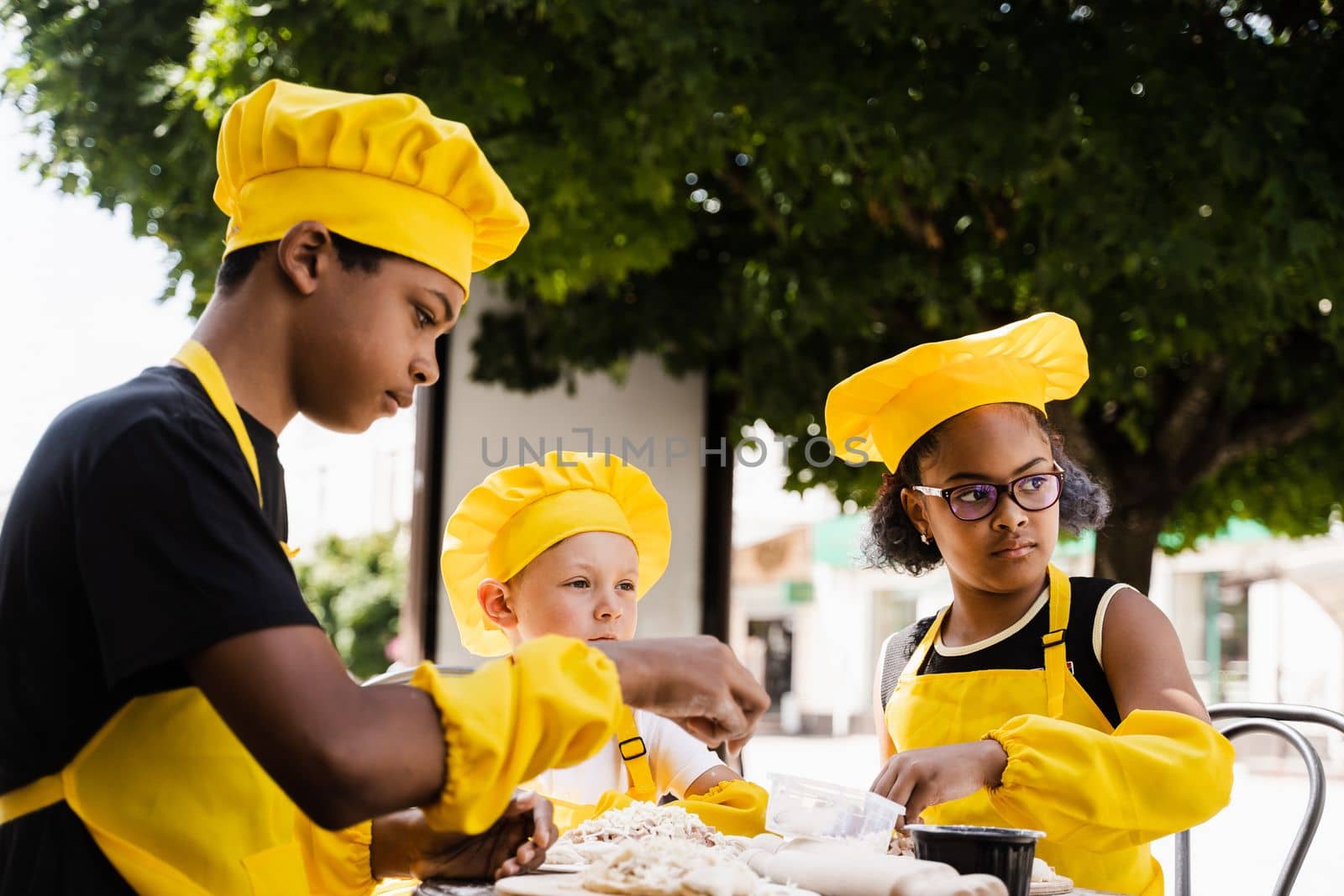 Happy company of multiethnic children cooking dough. Childhood cook activity of multinational children of black african and caucasian kids. by Rabizo