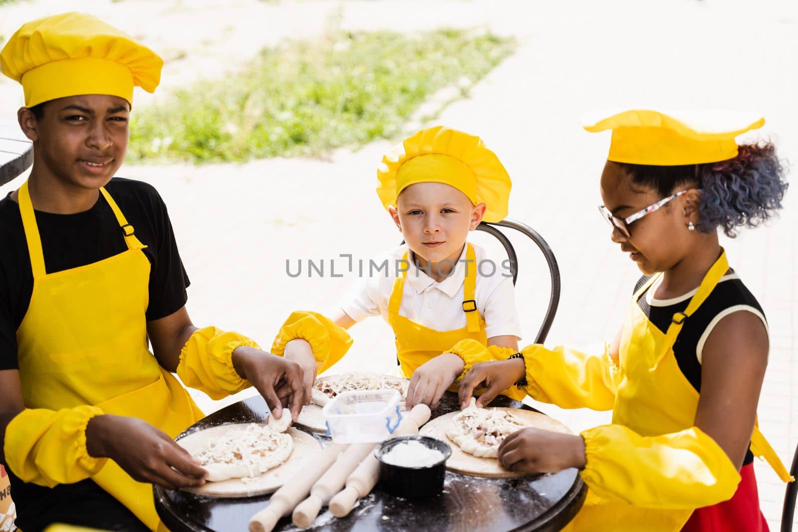 Childhood cook activity of multinational children of black african and caucasian kids in yellow chefs hat and apron uniform. Happy company of multiethnic children cooking dough