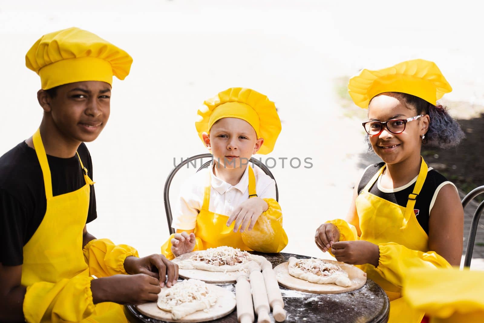 Childhood cook activity of multinational children of black african and caucasian kids in yellow chefs hat and apron uniform. Happy company of multiethnic children cooking dough