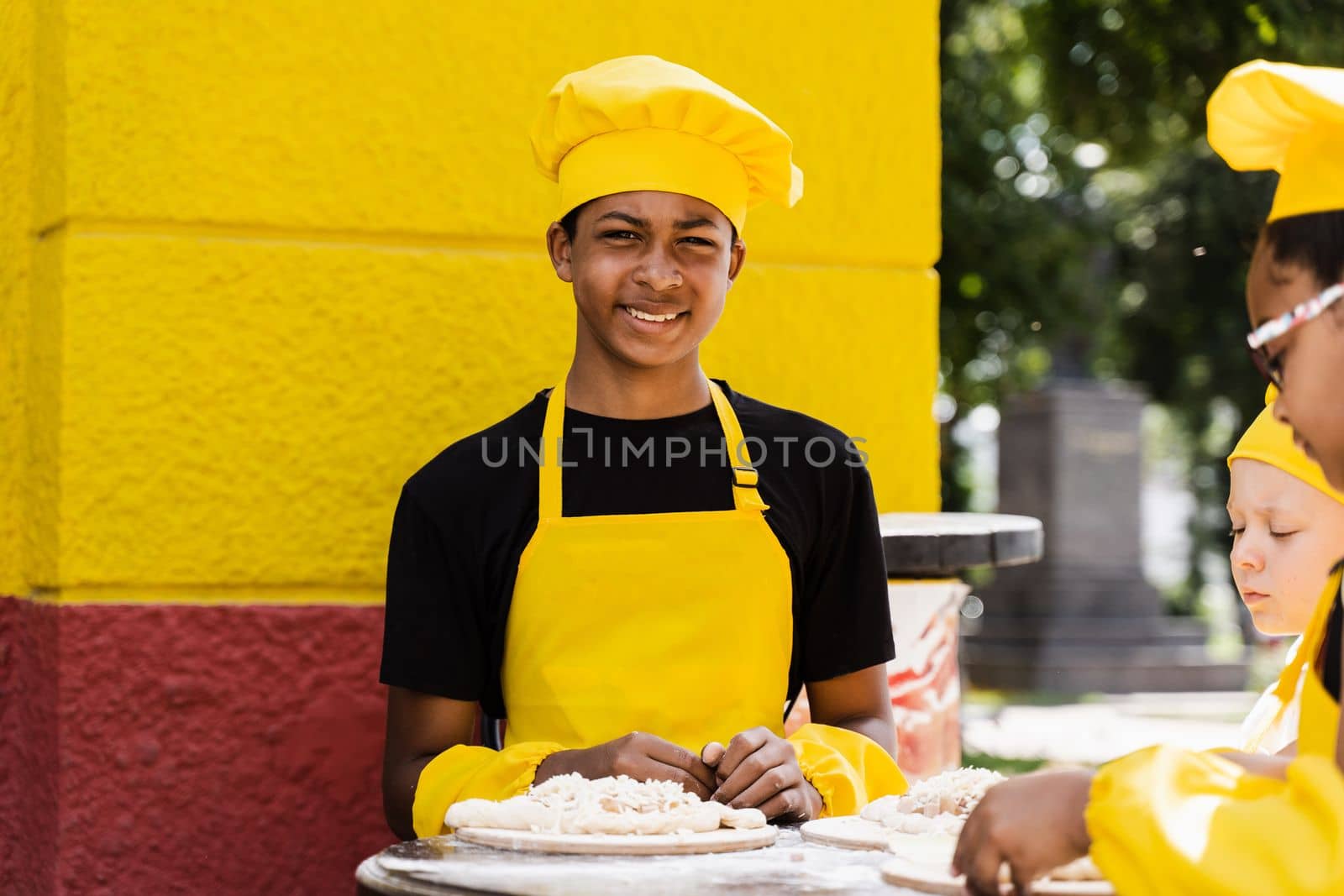 Black african teenager cook in chefs hat and yellow apron uniform cooking dough for bakery. Creative advertising for cafe or restaurant