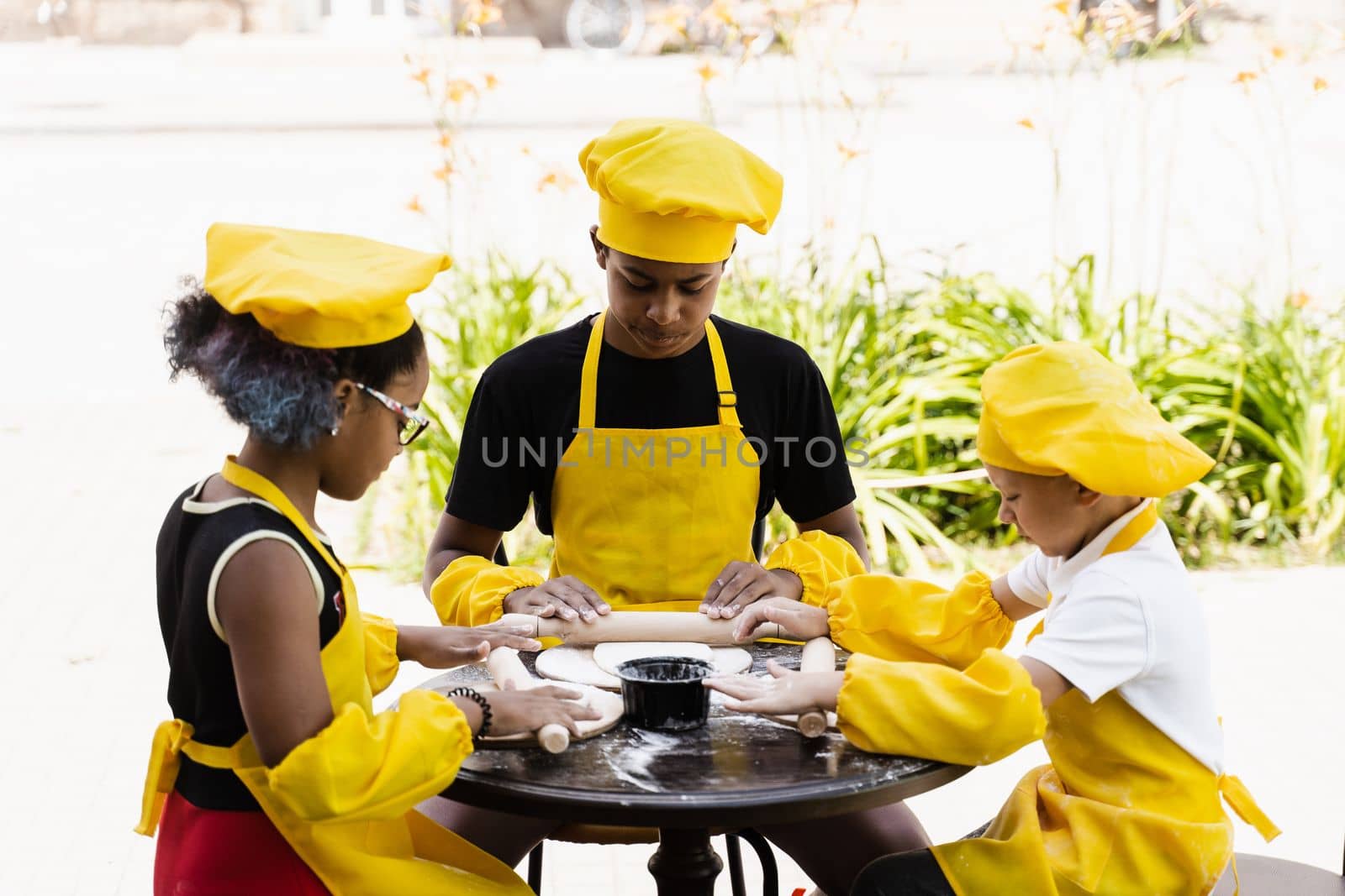 Multinational company of children cooks in yellow uniforms cooking dough for bakery. African teenager and black girl have fun with caucasian child boy and cook food