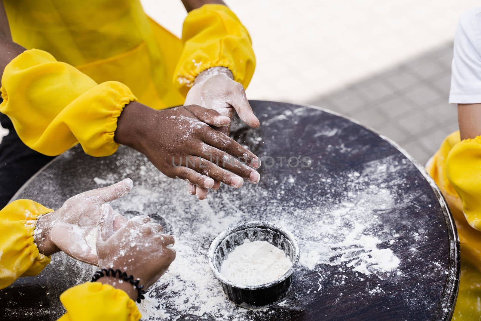 Hands of multinational children cooks play with flour for dough and having fun close-up. Young cooks children cooking khachapuri.