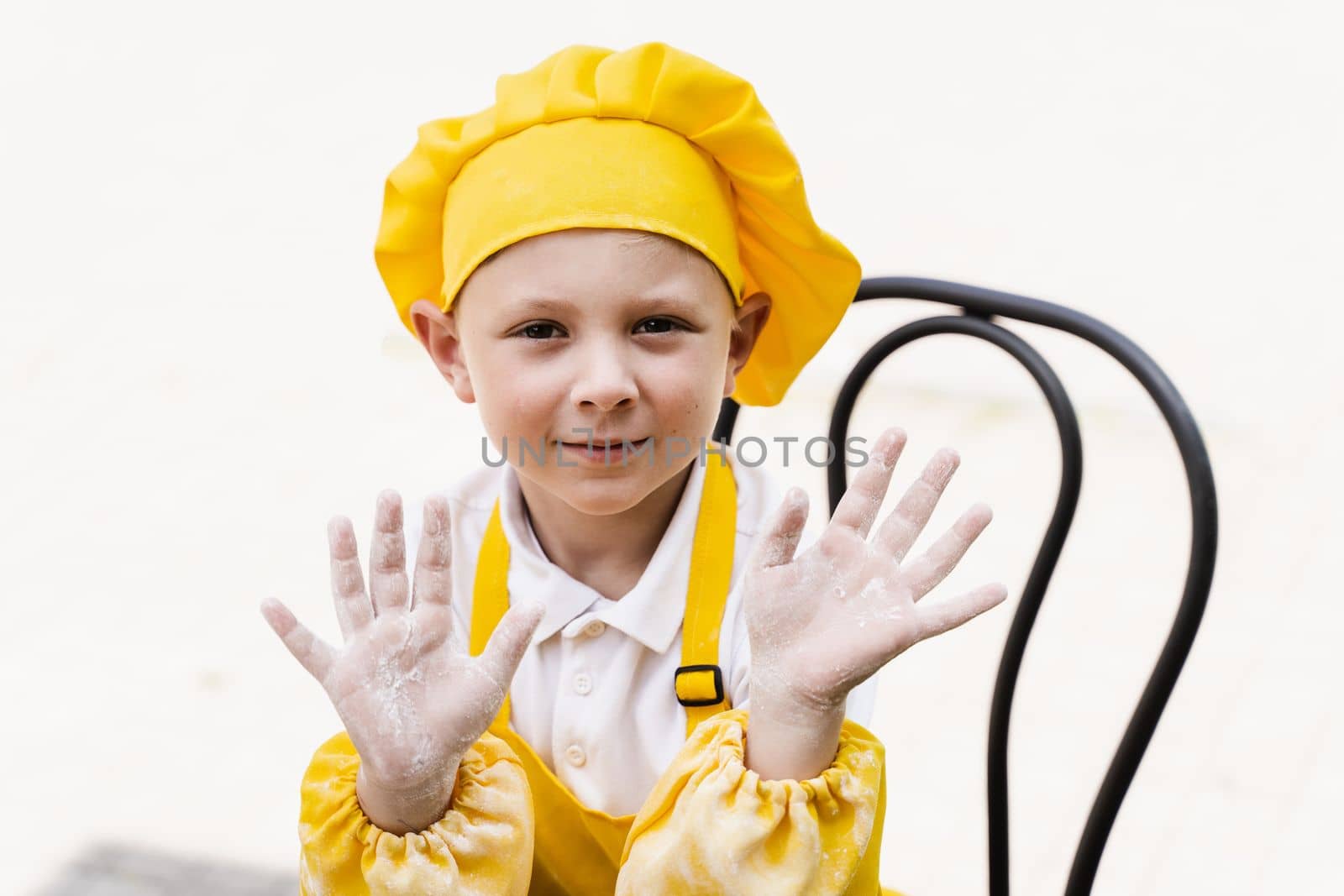 Attractive cook child boy showing hands with flour and smile. Caucasian child in chefs hat and yellow apron uniform