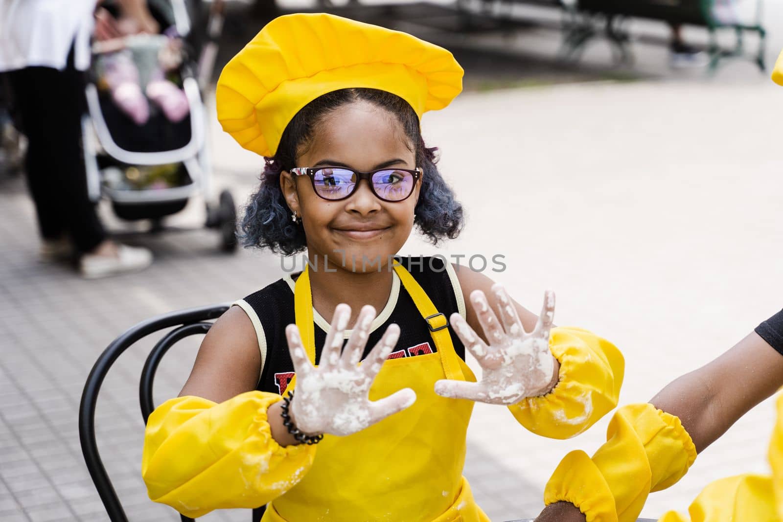 Black african cook child girl showing hands with flour and smile. African child in chefs hat and yellow apron uniform
