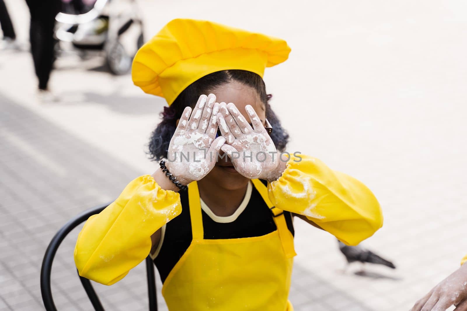 Black african cook child girl showing hands with flour and close her face. African child in chefs hat and yellow apron uniform
