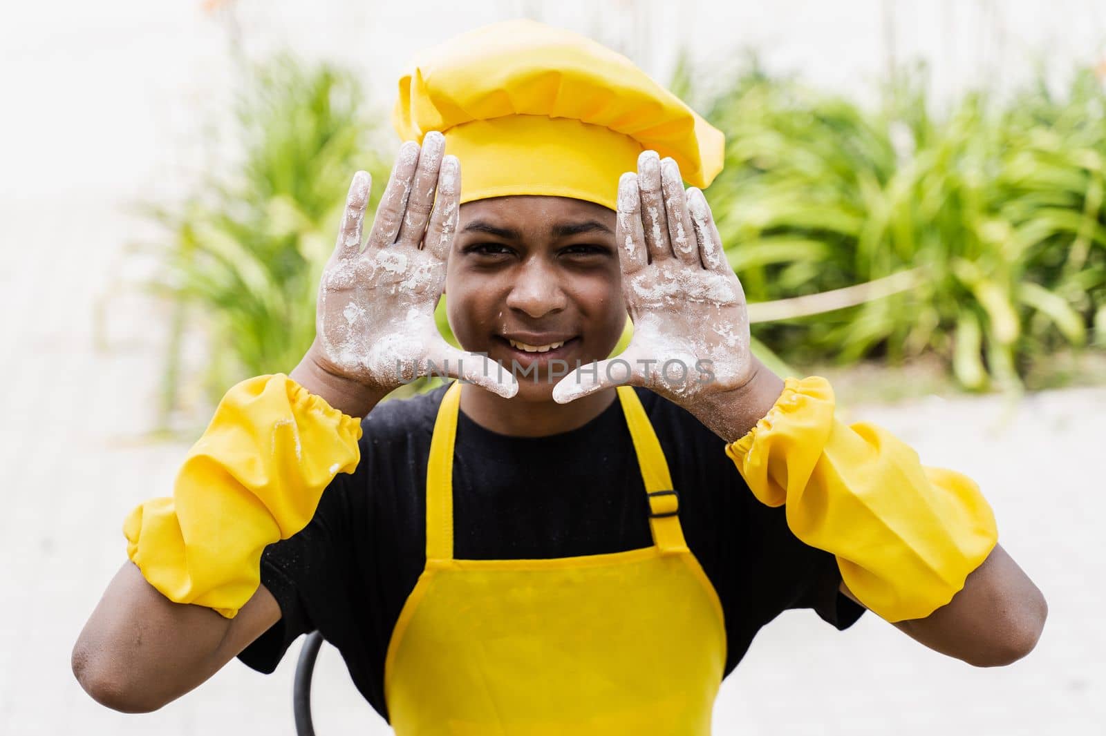 Black african cook teenager showing hands with flour and smiling. African child in chefs hat and yellow apron uniform