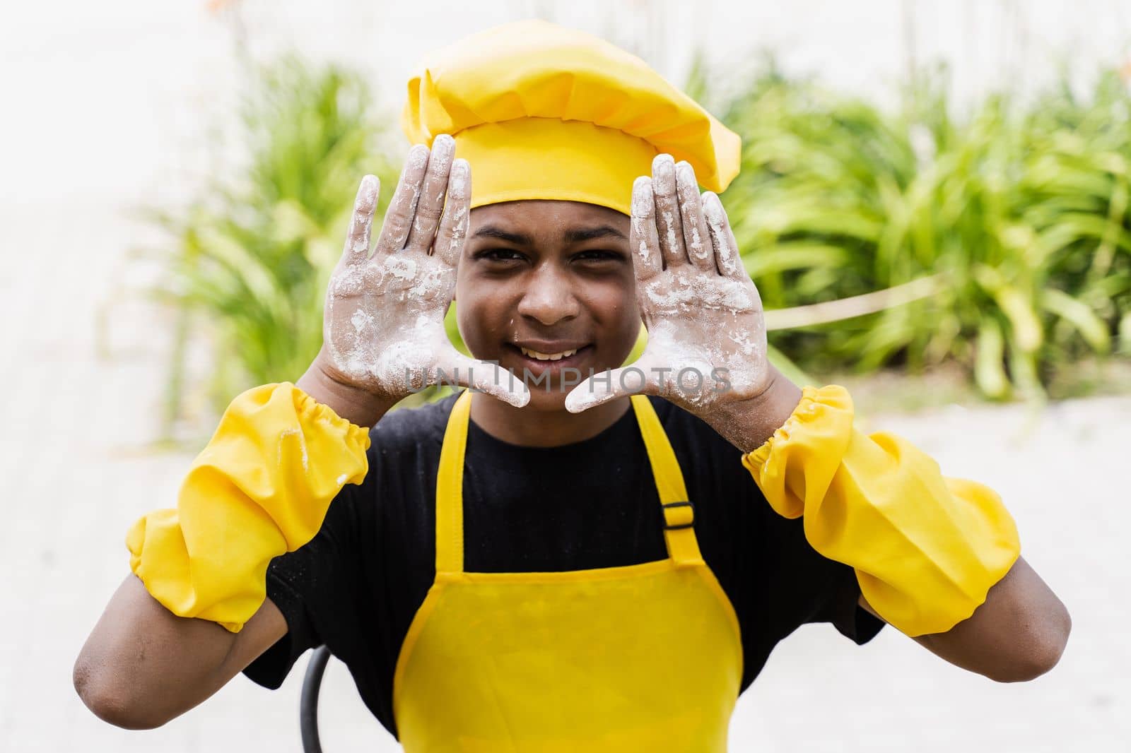 Black african cook teenager showing hands with flour and smiling. African child in chefs hat and yellow apron uniform. by Rabizo