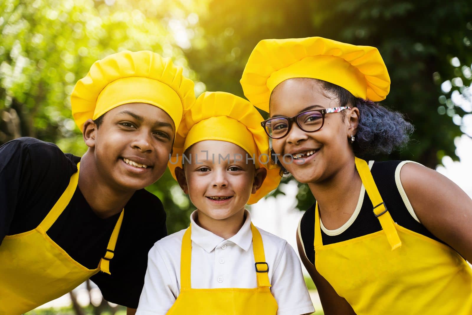 Multiracial company of children cooks in yellow uniforms smile outdoor. African teenager and black girl have fun with caucasian child boy and cook food. Kids portrait. by Rabizo