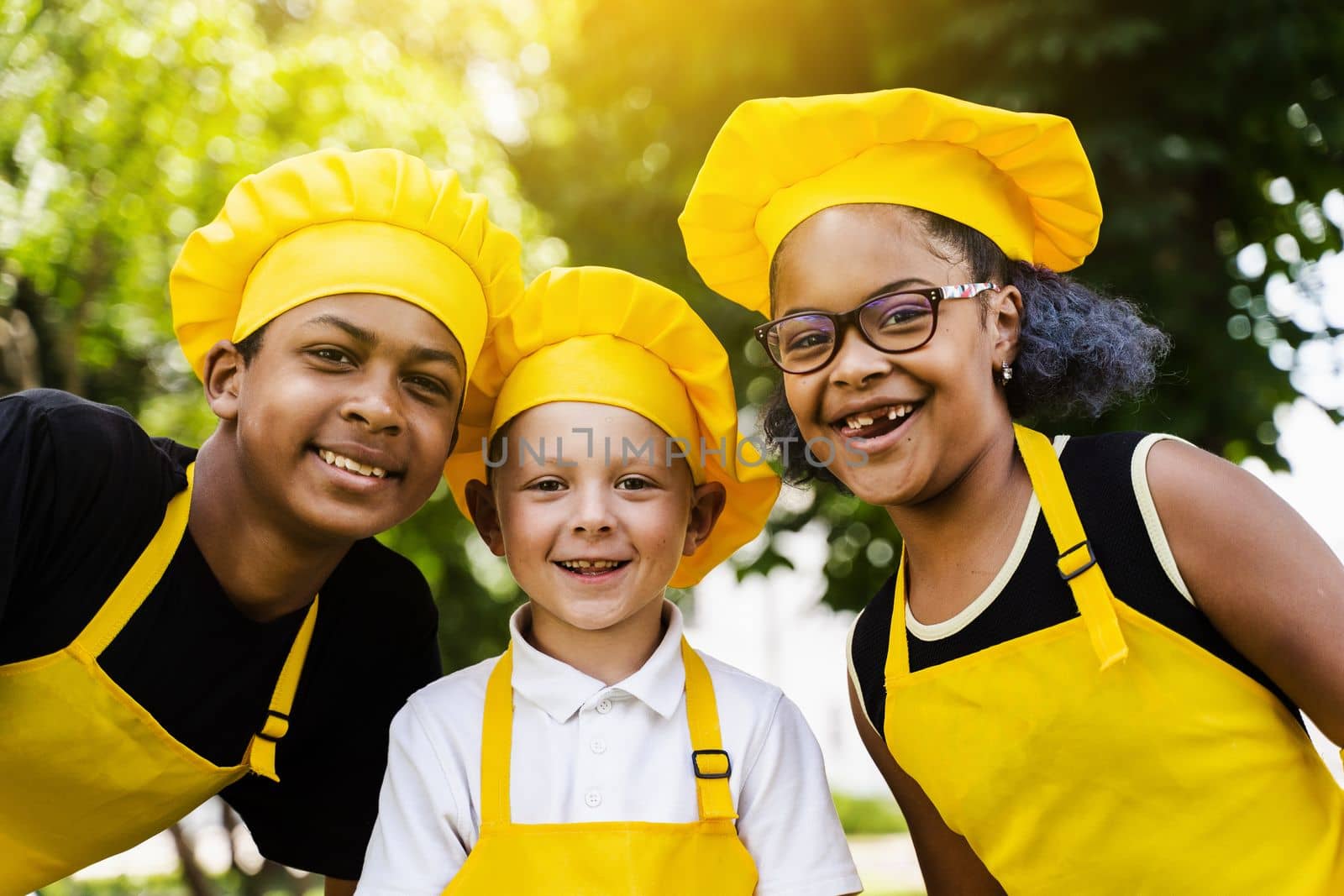 Multiracial company of children cooks in yellow uniforms smile outdoor. African teenager and black girl have fun with caucasian child boy and cook food. Kids portrait