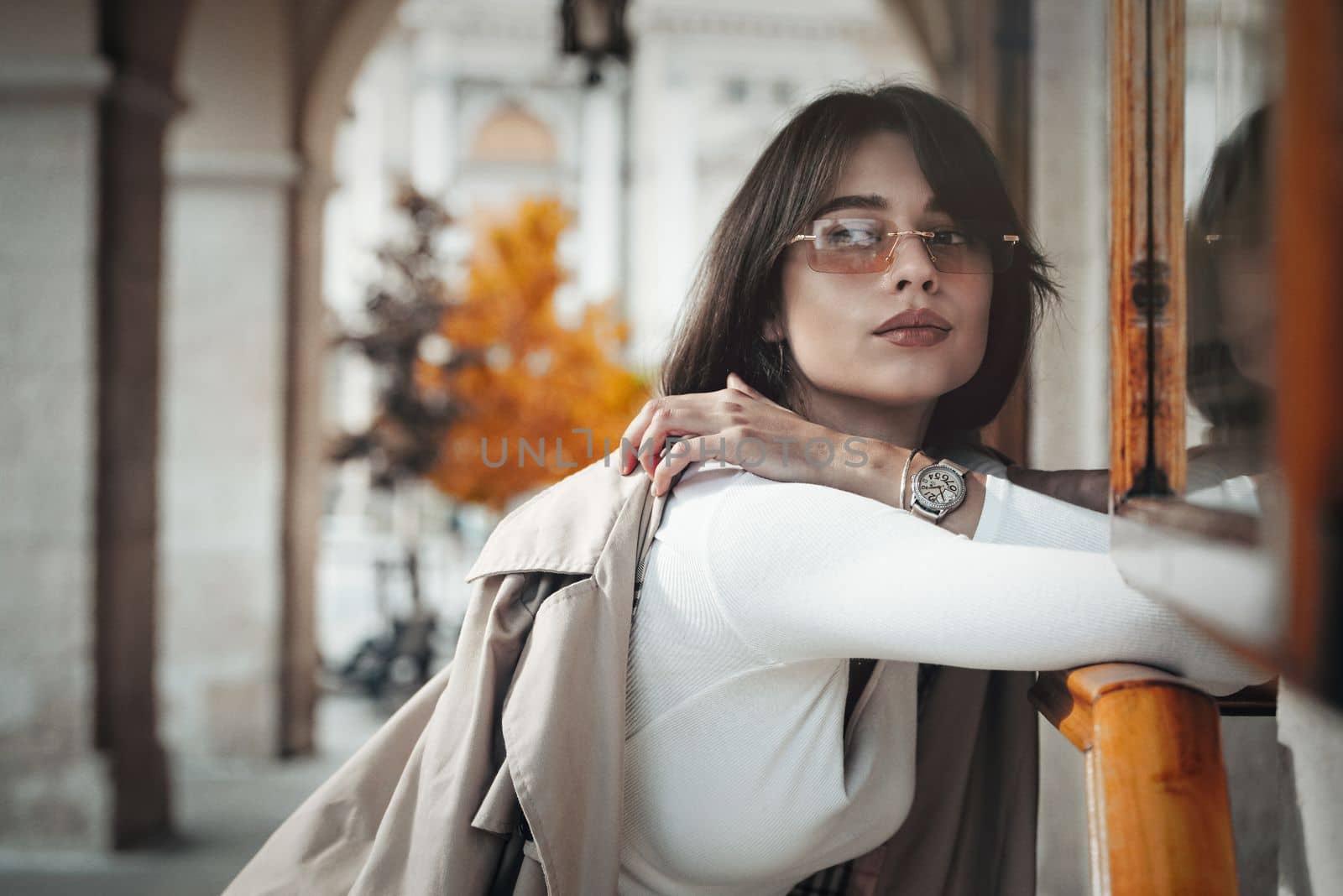 beautiful brunette girl in a sunglasses dressed in white blouse with a beige coat in hands. Stylish trendy fashion outlook by Ashtray25