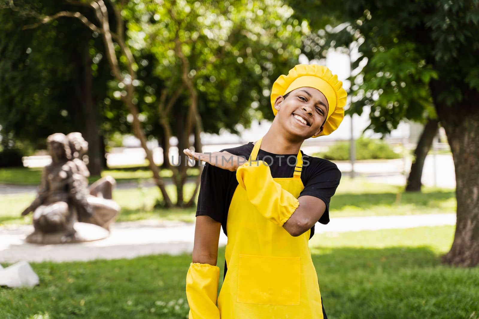 Happy black african teenager cook in chefs hat and yellow apron uniform smiling outdoor. Creative advertising for cafe or restaurant. by Rabizo