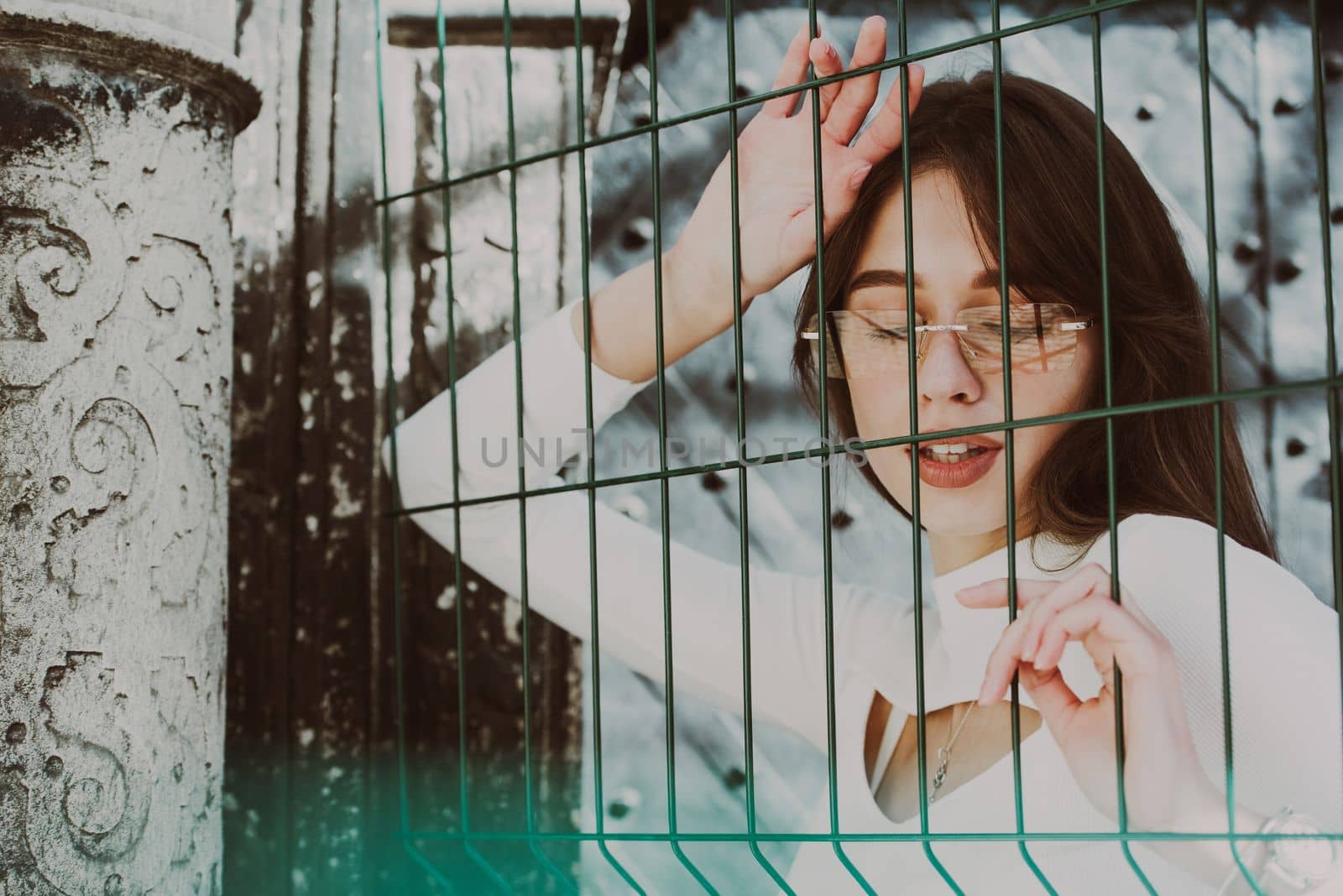 Close-up portrait of woman a in a white blause near a green metal grid