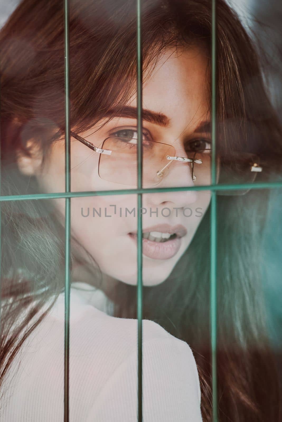 Close-up portrait of woman a in a white blause near a green metal grid