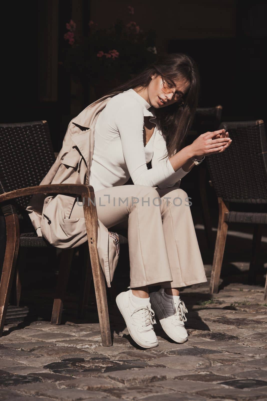 beautiful brunette girl dressed in white blouse, pants, sneakers with a handbag and camel coat in hands. Stylish trendy fashion outlook by Ashtray25