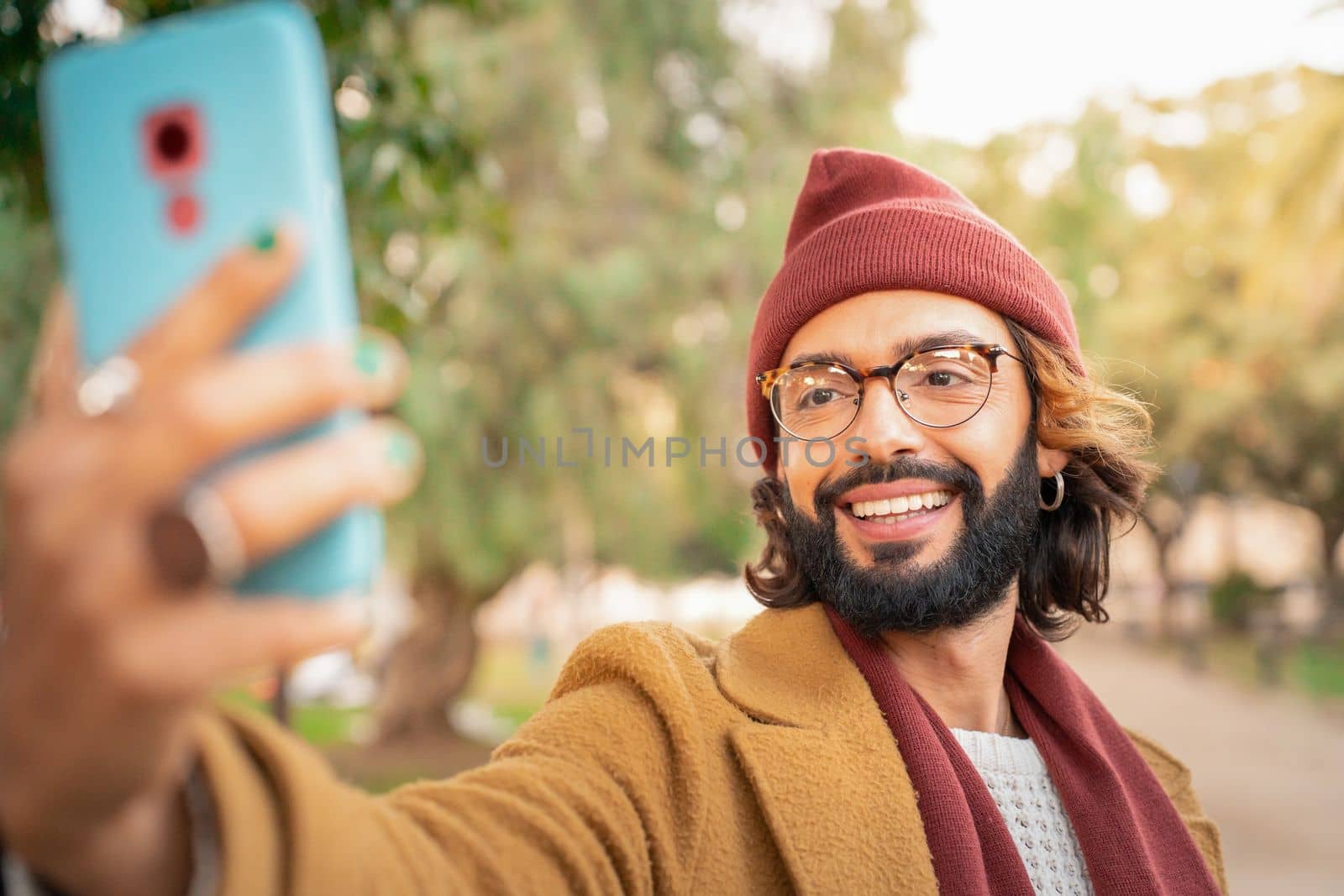 Attractive young caucasian man with glasses and beard taking a selfie outdoors in the park. Happy smiling video call. Technology and communication concept.