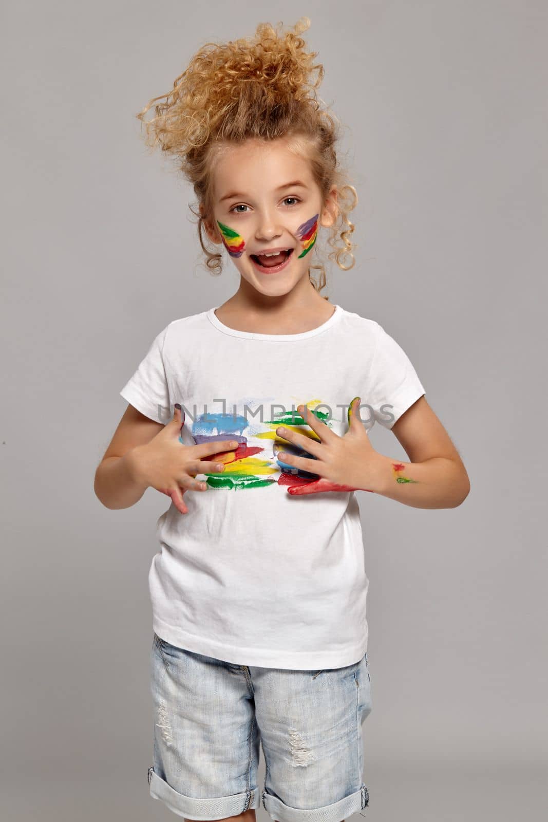 Nice little lady having a brush in her lovely haircut, wearing in a white t-shirt. She is smearing her t-shirt and looking happy on a gray background.