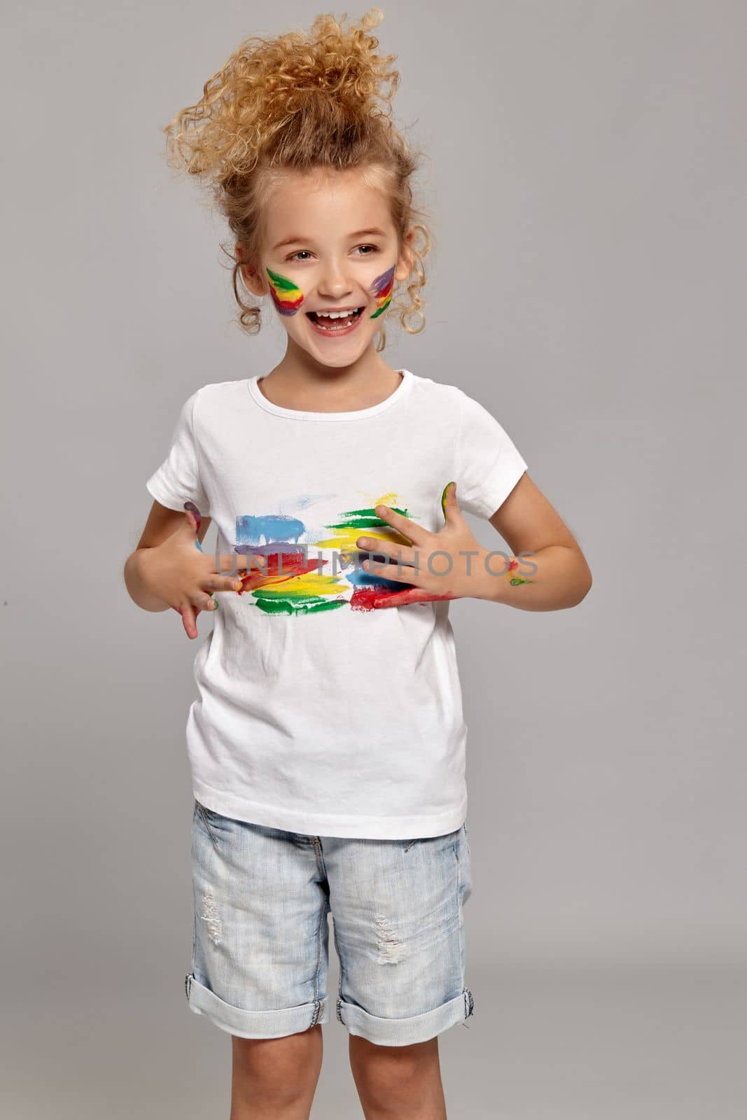 Wonderful little girl having a brush in her lovely haircut, wearing in a white t-shirt. She is smearing her t-shirt, laughing and looking away, on a gray background.