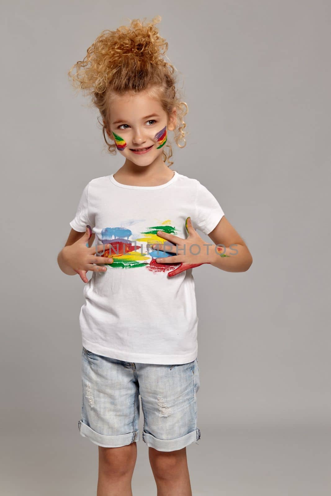 Wonderful child having a brush in her lovely haircut, wearing in a white t-shirt. She is smearing her t-shirt, smiling and looking away, on a gray background.