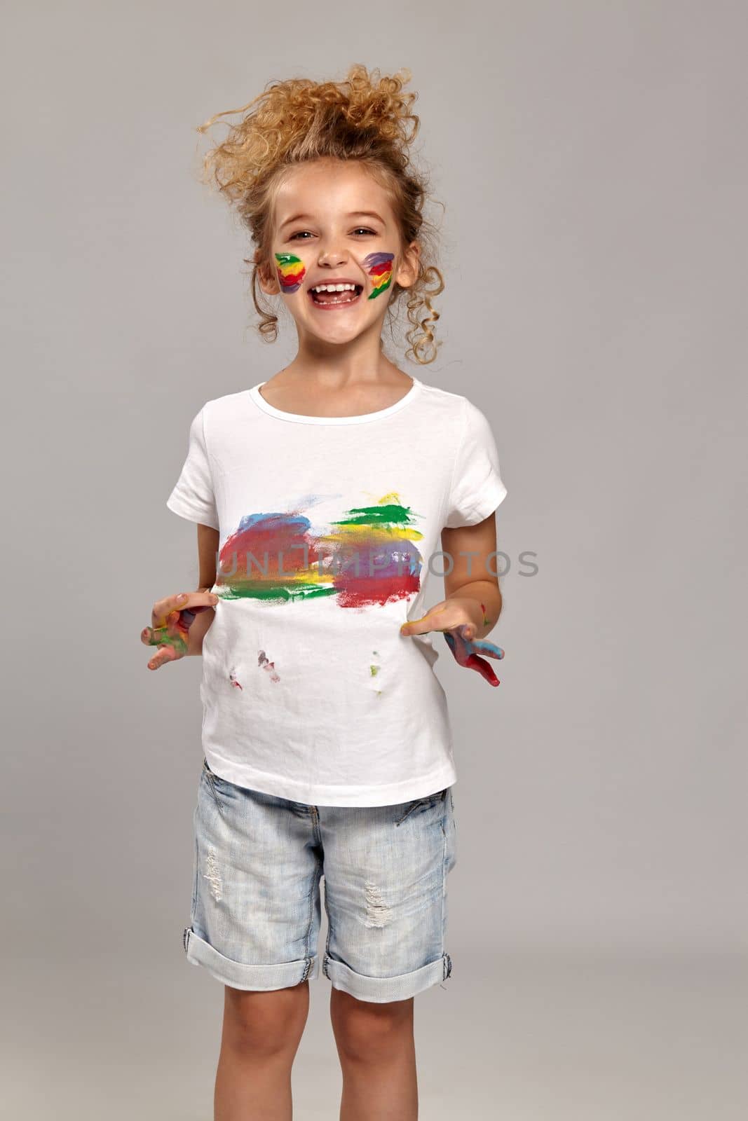 Beautiful child having a brush in her lovely haircut, wearing in a white smeared t-shirt. She is holding it and looking very happy, on a gray background.