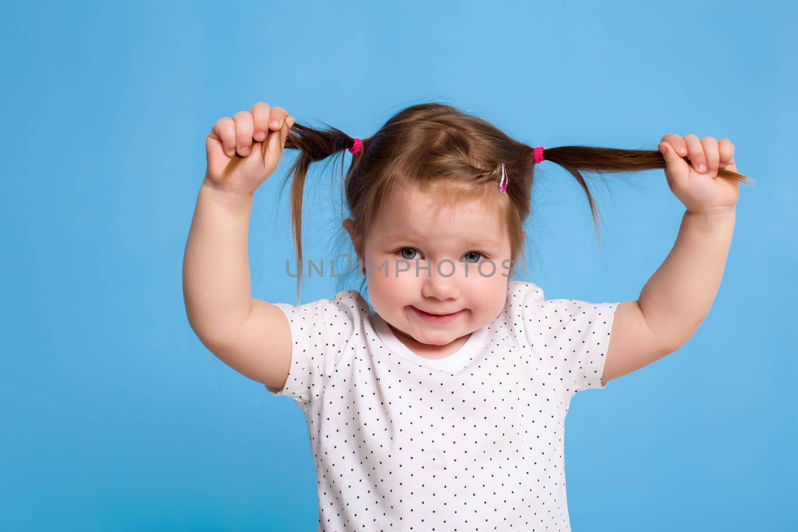 Funny kid in white T-shirt on blue background. Little pretty girl holding on to the tails. Copy space for text. Sale, birthday party concept.